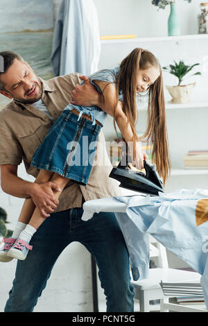 Father carrying désobéissante fille et elle vouloir repasser les vêtements à la maison Banque D'Images