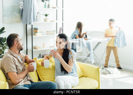 Vêtements Enfants planche tandis que les parents de boire du café à la maison Banque D'Images