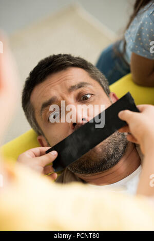 Portrait d'enfants terminant père bouche avec du ruban adhésif noir à la maison Banque D'Images