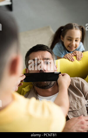 Vue aérienne d'enfants terminant père bouche avec du ruban adhésif noir à la maison Banque D'Images