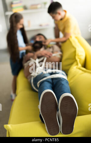 La fermeture de la bouche des enfants père avec ruban noir à la maison avec les pieds sur le premier plan Banque D'Images