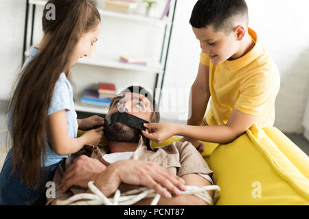 Les enfants désobéissants père clôture la bouche avec du ruban adhésif noir à la maison, concept planning Banque D'Images