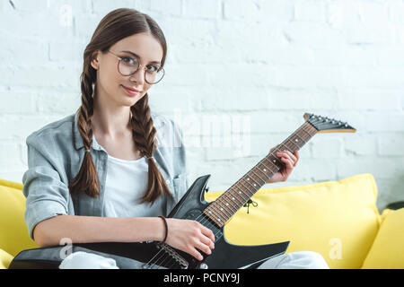 Une adolescente attrayant playing electric guitar on sofa at home Banque D'Images