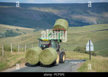 Premier tracteur big bales de l'ensilage dans une petite route rurale près de Hoggarths dans Swaledale, North Yorkshire, UK. Banque D'Images
