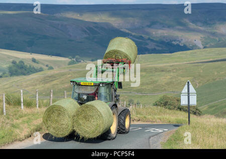 Premier tracteur big bales de l'ensilage dans une petite route rurale près de Hoggarths dans Swaledale, North Yorkshire, UK. Banque D'Images