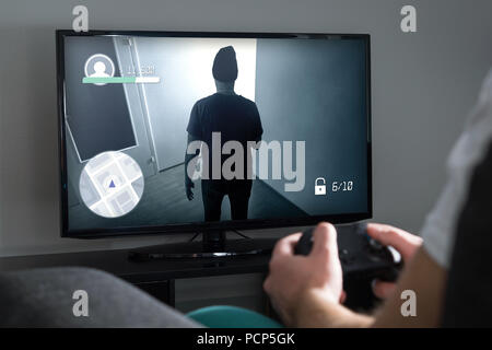 Jouer à des jeux vidéo à la maison avec la console. Avec contrôleur de joueur ou une manette en main. Jeune homme et d'une télévision avec jeux d'action à l'écran. Banque D'Images