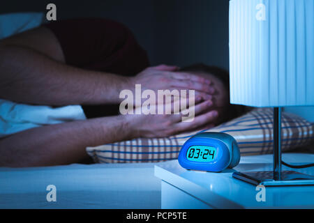 Voir cauchemars et mauvais rêves concept. L'homme effrayé couvrant le visage avec les mains au lit. Réveil sur table de nuit dans la chambre. Banque D'Images