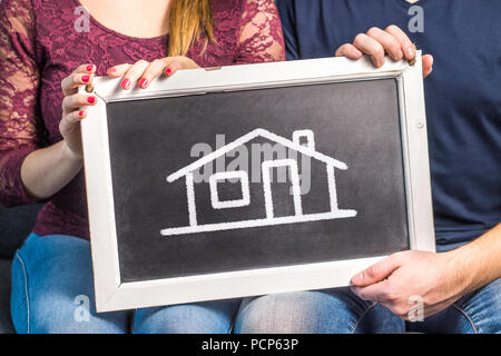 Maison de rêve, l'assurance habitation, de design d'intérieur ou la planification future concept. Heureux couple, homme et femme, holding blackboard with dessinés de maison. Banque D'Images