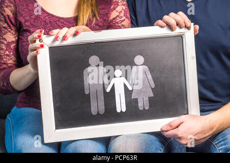 Avoir des enfants, la planification bébé, élever des enfants, d'adoption, de filiation ou concept d'infertilité. Man and Woman holding tableau noir avec la famille. Banque D'Images