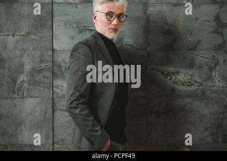 Portrait of businessman standing contre fond gris. Beau mâle debout avec ses mains dans les poches et en regardant la caméra. Banque D'Images