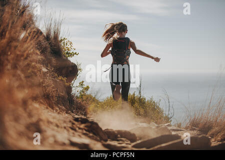 Vue arrière de l'exécution de femmes sur des sentiers rocailleux sur la colline. Trail Runner tournant en descente. Banque D'Images