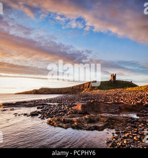 Château de Dunstanburgh, maintenant une ruine, commandant la plage à Embleton Bay, Northumberland, Angleterre, sous un ciel aube dramatique. Banque D'Images