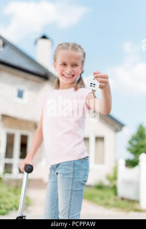 Enfant souriant avec le scooter de coup maintenant la touche avec trinket près de new house Banque D'Images