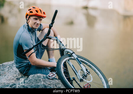 Jeune motard de première détente sur une falaise rocheuse au-dessus de l'eau et looking at camera Banque D'Images