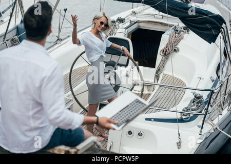 High angle view of smiling girl au volant de forme main et regardant jeune homme on yacht Banque D'Images