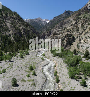 Rivière coule vers le bas d'une montagne du Wyoming vallée bordée de vert des arbres. Banque D'Images