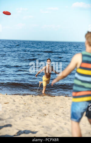 Portrait de jeunes hommes jouant avec flying disc on sandy beach Banque D'Images