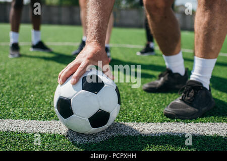 Vue partielle de l'ancien player holding football ball avec amis multiraciale derrière le terrain de football Banque D'Images