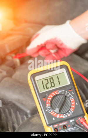 Mécanicien automobile utilise un multimètre pour vérifier la tension de la batterie de voiture Banque D'Images