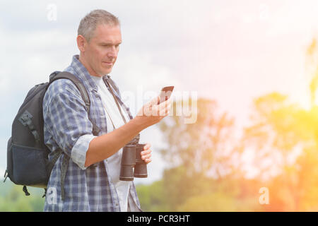 Homme backpacker using smart phone et holding binoculars Banque D'Images