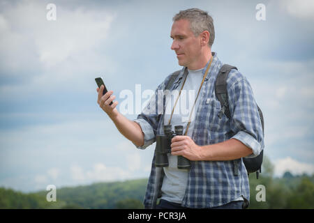 Homme backpacker using smart phone et holding binoculars Banque D'Images