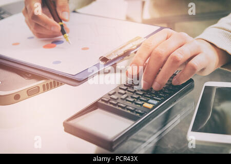 Tenir la main de femme calculatrice et écrit avec un stylo, financiers et rapport graphique portable sur 24 au bureau. Banque D'Images