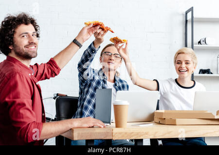 Happy young businesswoman eating pizza and smiling at camera Banque D'Images