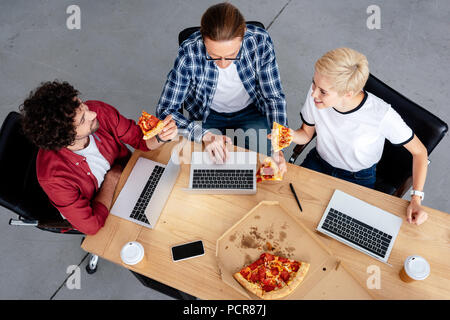 Vue de dessus de jeunes collègues de manger des pizzas et à l'aide d'un ordinateur portable sur le lieu de travail Banque D'Images