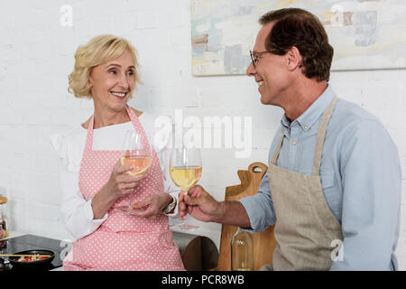 Heureux en couple de tabliers et souriant les uns les autres dans la cuisine Banque D'Images