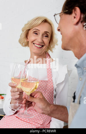 Happy senior couple de tabliers clinking verres de vin pendant la cuisson ensemble Banque D'Images