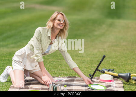 Happy young woman putting couverts sur plaid at picnic Banque D'Images