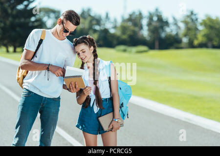 Les adolescents heureux holding books en position debout et smiling together in park Banque D'Images