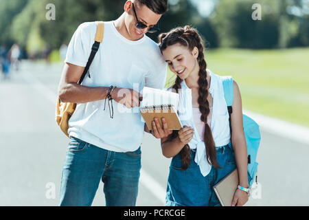 Heureux les adolescents avec des sacs holding books en position debout et smiling together in park Banque D'Images