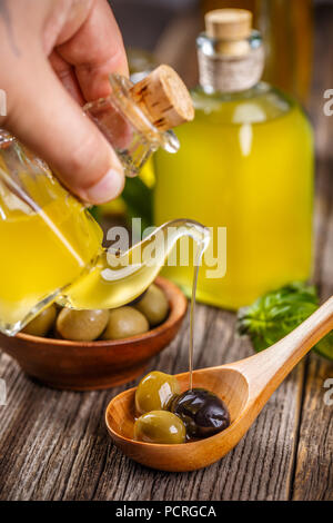L'huile d'olive extra vierge flux sur une cuillère en bois plein d'olives vertes et noires Banque D'Images
