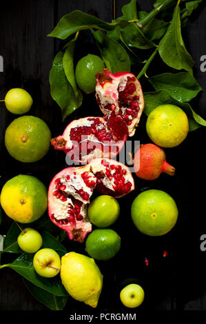 citron sur une branche et des limes. grenade hachée. sur fond noir. photo sombre. gouttes d'eau. fruits mouillés. Banque D'Images