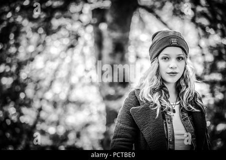 Jeune fille à l'extérieur avec cap, portrait dans la forêt, à la recherche au sérieux dans l'appareil photo, image en noir et blanc Banque D'Images