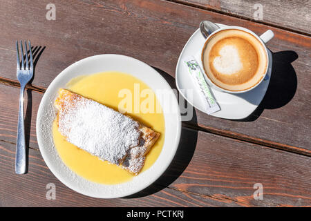 Apple strudel traditionnel avec de la sauce à la vanille et cappuccino servi au refuge de montagne de Gênes, Schlüterhütte Funes Valley, parc naturel de Puez-Geisler, Dolomites, Bolzano, le Tyrol du Sud, Italie Banque D'Images