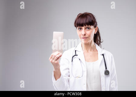 Femme médecin détenant un téléphone mobile à la main, avec un air pensif et un stéthoscope autour du cou Banque D'Images