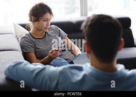 Young hispanic couple portant sur la table à la maison, à l'aide d'un tablet PC et carte de crédit pour l'achat en ligne. Le petit ami est de donner un massage aux pieds de Banque D'Images