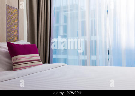 Une bande rose oreiller sur lit blanc dans une chambre à coucher, brighly allumé avec grande fenêtre de taille, prix pour copy space Banque D'Images