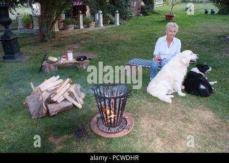 Jeune femme blonde est assise avec ses chiens par le feu de camp Banque D'Images