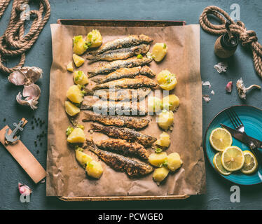 Sardines grillées avec des pommes de terre sur la plaque de cuisson avec des ingrédients : citron, ail et herbes pour manger des fruits de mer savoureux. Préparation Cuisson des poissons Banque D'Images