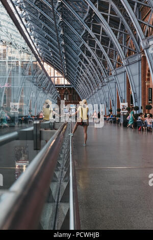 Femme non identifiée dans un haut jaune à parler au téléphone à l'intérieur de St Pancras Station, London, UK. Banque D'Images