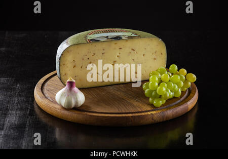 Morceau de fromage aux truffes, gousse d'ail et les raisins sur planche de bois sur fond noir Banque D'Images