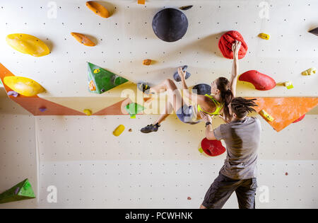 Grimpeurs en escalade. Jeune femme escalade bouldering problème (route) sur le mur en surplomb, de sécuriser les instructeurs masculins. Banque D'Images