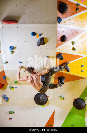 Jeune homme difficile escalade bouldering itinéraire. Dans la salle d'escalade intérieure. Banque D'Images
