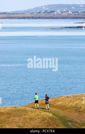 Le Nord du Pays de Galles, Royaume-Uni Météo : Temps chaud et ensoleillé renvoie à de nombreuses parties de l'UK ce week-end en ces deux hommes joggers découvert exécutant alonge le sentier du littoral à Nobla Porth sur Anglesey Banque D'Images