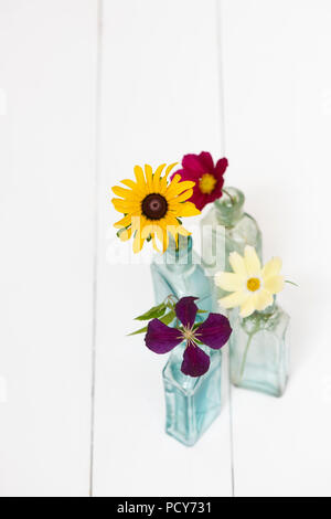 Fleurs cueillies dans des bouteilles en verre vintage sur fond blanc Banque D'Images