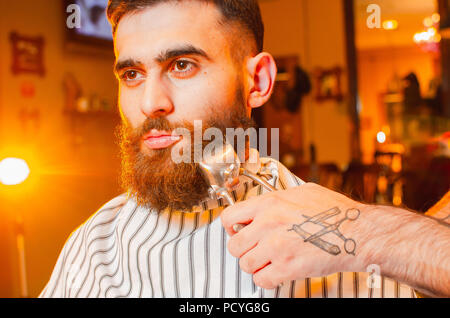 Coiffure Coupe une barbe de tondeuses à cheveux vintage à un jeune beau gars avec une barbe et moustache. Salon de coiffure pour hommes. Banque D'Images