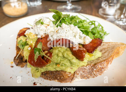 Assiette sur la table du restaurant ; pain grillé au levain recouvert d'avocat écrasé, de fromage feta et de chorizo, Royaume-Uni Banque D'Images